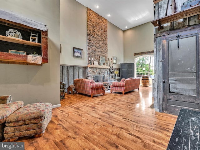 living room with a stone fireplace, a towering ceiling, and wood-type flooring