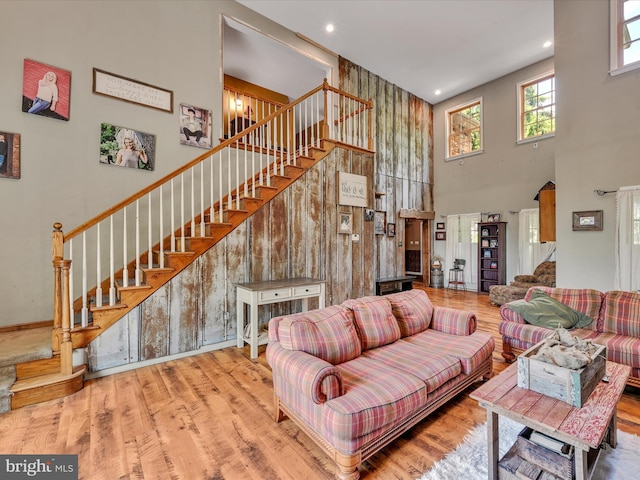 living room featuring a towering ceiling, light hardwood / wood-style flooring, and wood walls