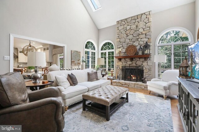 living room featuring a stone fireplace, a skylight, high vaulted ceiling, and light hardwood / wood-style flooring