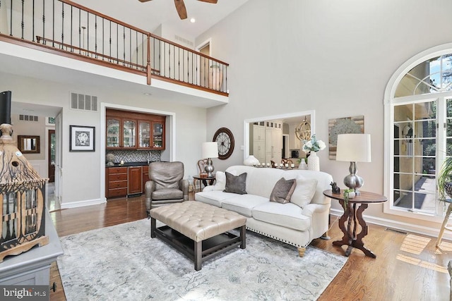 living room featuring bar, hardwood / wood-style floors, a towering ceiling, and ceiling fan