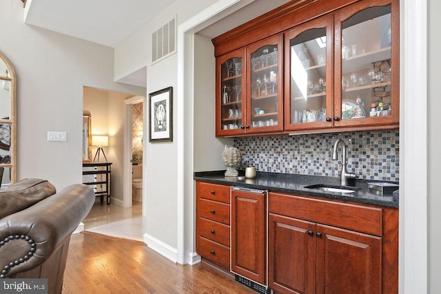 bar featuring tasteful backsplash, sink, dark stone counters, and wood-type flooring