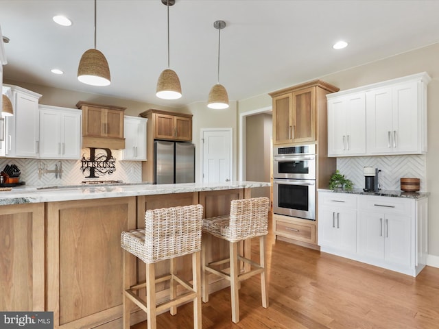 kitchen with white cabinets, appliances with stainless steel finishes, light hardwood / wood-style floors, and decorative backsplash