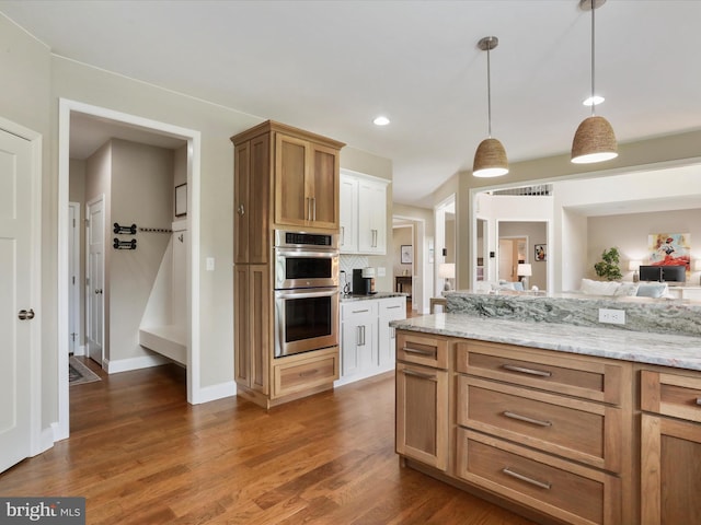 kitchen featuring double oven, light stone counters, dark wood-type flooring, and hanging light fixtures