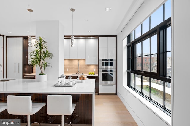 kitchen with decorative light fixtures, white cabinetry, light wood-type flooring, and tasteful backsplash