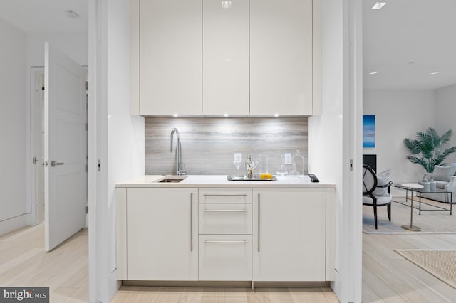 bar with light hardwood / wood-style flooring, white cabinets, and sink