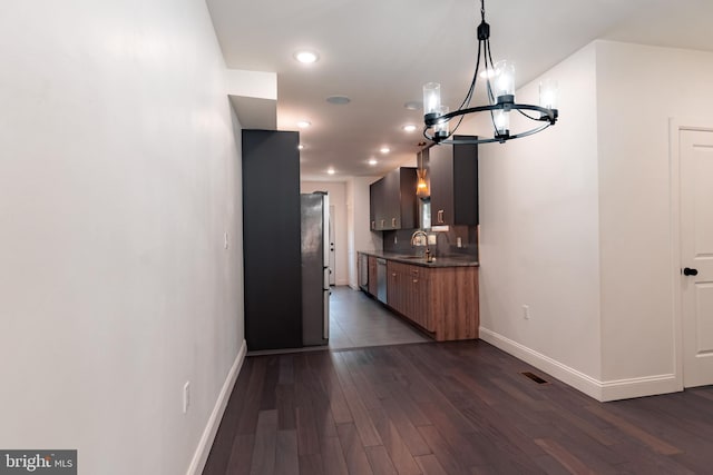 kitchen featuring sink, dark wood-type flooring, stainless steel appliances, an inviting chandelier, and pendant lighting