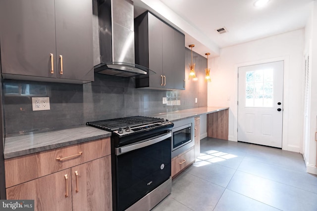 kitchen featuring decorative backsplash, dark stone counters, wall chimney exhaust hood, stainless steel appliances, and decorative light fixtures