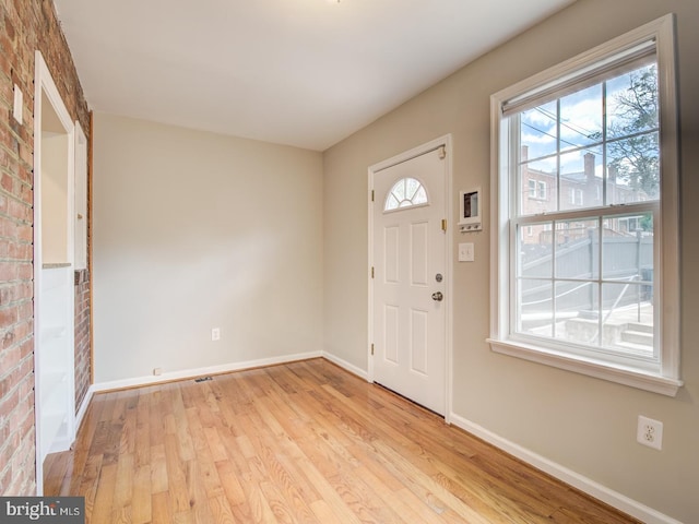 foyer with light wood-type flooring and brick wall