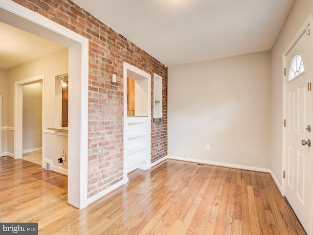 foyer entrance with light hardwood / wood-style floors and brick wall