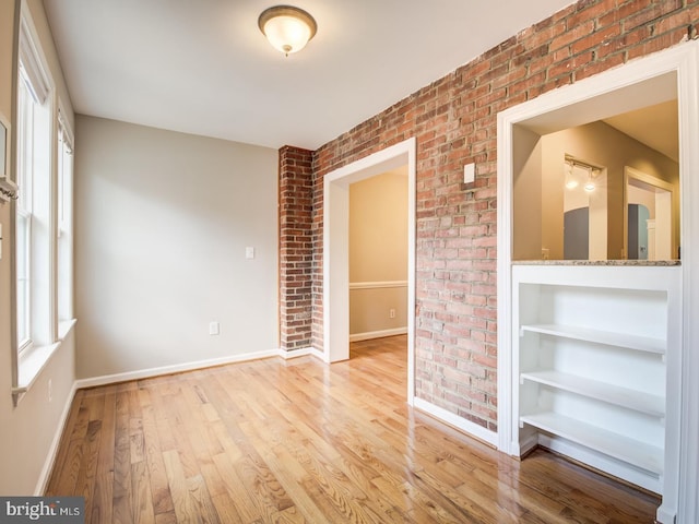 empty room with plenty of natural light, brick wall, and light wood-type flooring