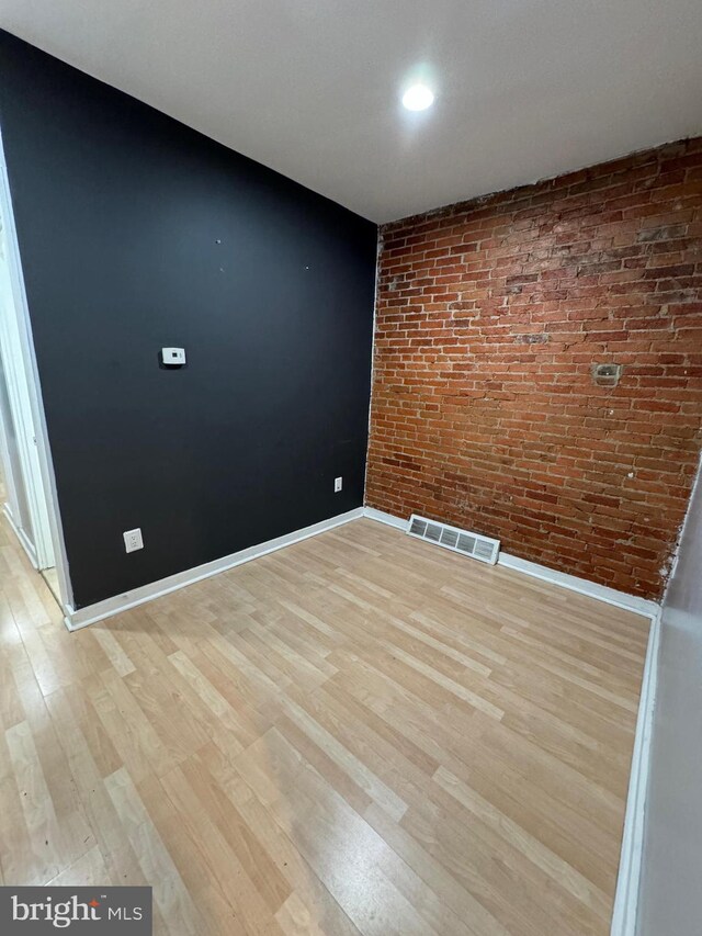 spare room featuring brick wall and light hardwood / wood-style flooring