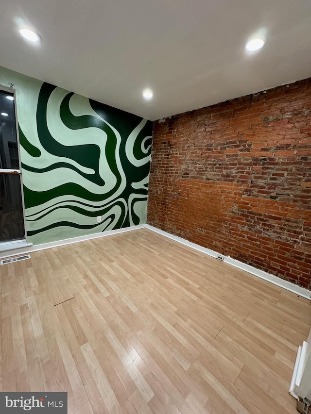 empty room featuring wood-type flooring and brick wall