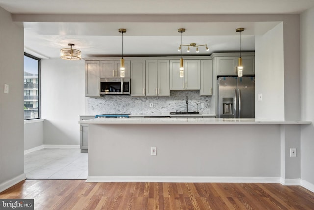 kitchen with appliances with stainless steel finishes, light wood-type flooring, decorative light fixtures, and sink