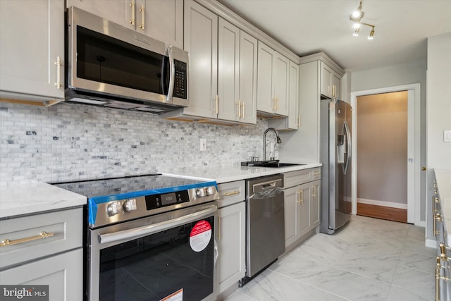 kitchen featuring appliances with stainless steel finishes, tasteful backsplash, light stone counters, sink, and gray cabinets