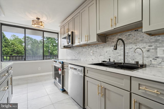 kitchen featuring light stone countertops, backsplash, gray cabinetry, stainless steel appliances, and sink