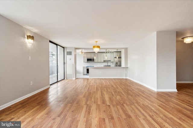 unfurnished living room with light wood-type flooring and a notable chandelier