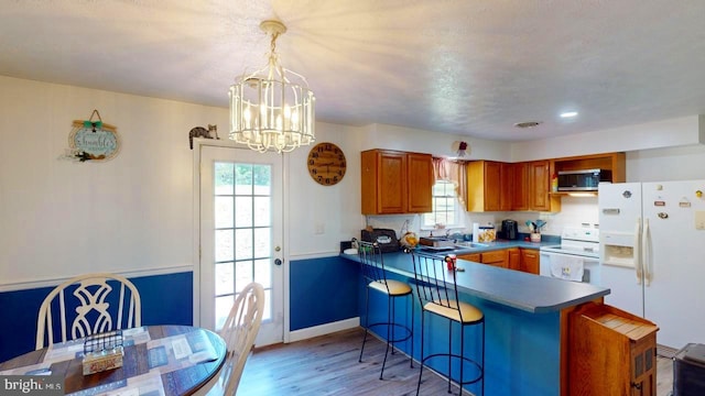 kitchen featuring kitchen peninsula, white appliances, a chandelier, light hardwood / wood-style floors, and hanging light fixtures