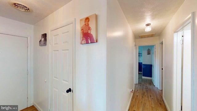 corridor with light wood-type flooring and a textured ceiling