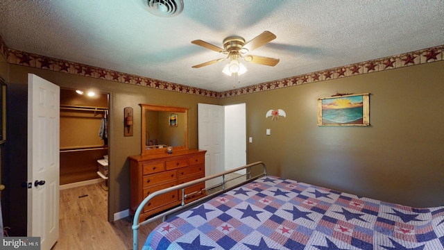 bedroom with a walk in closet, a textured ceiling, ceiling fan, light hardwood / wood-style flooring, and a closet