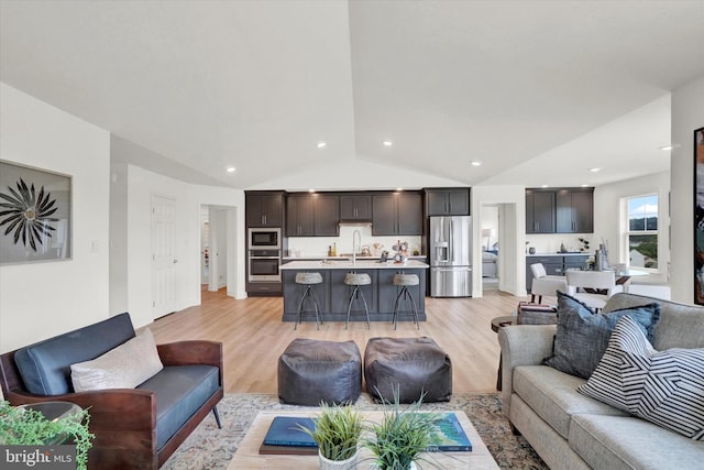 living room featuring sink, light hardwood / wood-style flooring, and vaulted ceiling