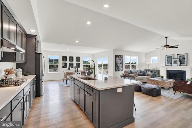 kitchen with lofted ceiling, a center island with sink, sink, light wood-type flooring, and appliances with stainless steel finishes