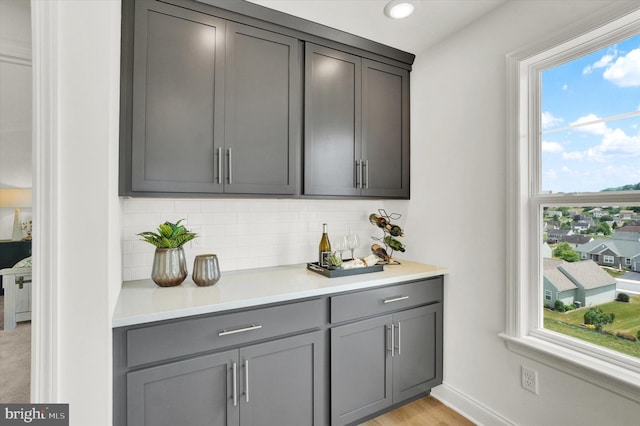 bar with gray cabinetry, decorative backsplash, and light hardwood / wood-style flooring