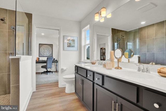 bathroom featuring a tile shower, toilet, vanity, and hardwood / wood-style flooring