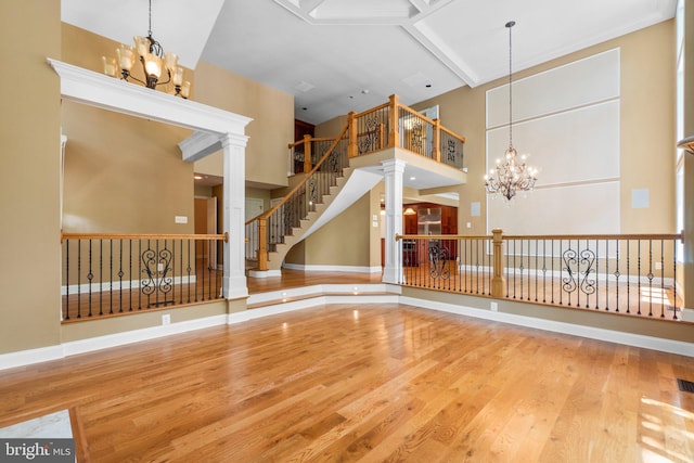 unfurnished living room with decorative columns, wood-type flooring, a high ceiling, and a notable chandelier