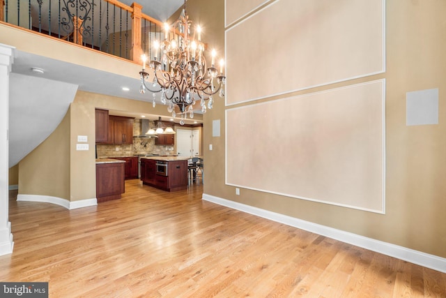 kitchen featuring light hardwood / wood-style floors, wall chimney exhaust hood, a center island, and a towering ceiling