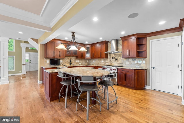 kitchen with light wood-type flooring, decorative columns, backsplash, wall chimney exhaust hood, and stainless steel stove