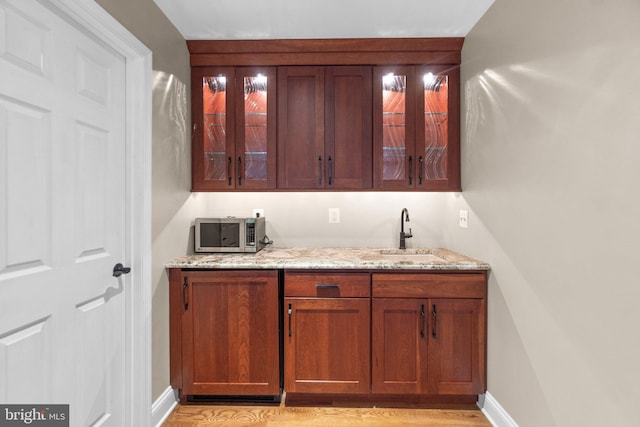 bar with light stone counters, light wood-type flooring, and sink