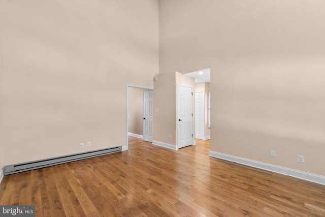 unfurnished room featuring baseboard heating, light hardwood / wood-style flooring, and a high ceiling