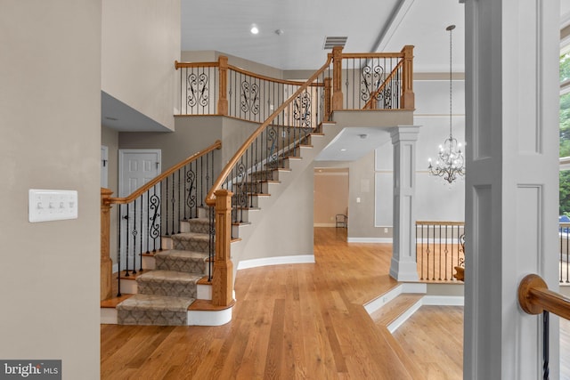 stairway featuring hardwood / wood-style floors, a notable chandelier, a towering ceiling, and ornate columns