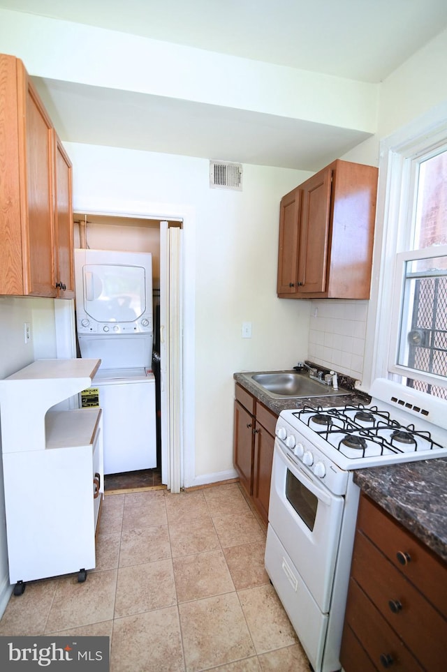 kitchen with stacked washing maching and dryer, tasteful backsplash, sink, white gas stove, and light tile patterned flooring