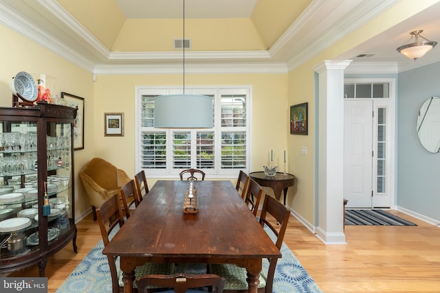 dining area with a tray ceiling, ornate columns, ornamental molding, and light hardwood / wood-style floors