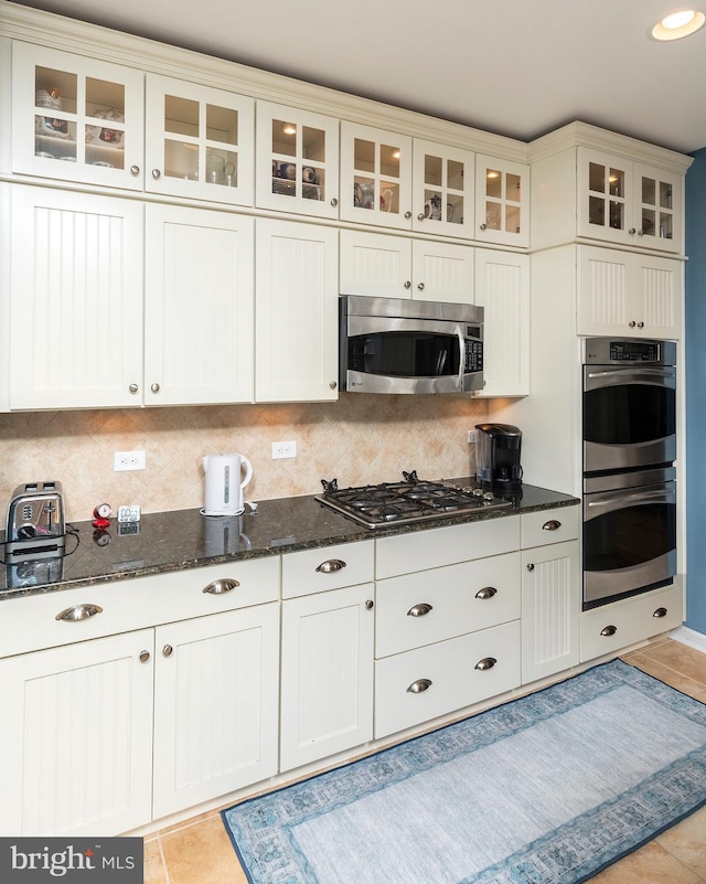 kitchen featuring dark stone counters, decorative backsplash, light tile patterned floors, and stainless steel appliances