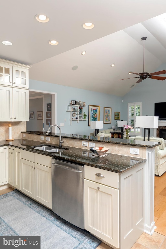 kitchen with sink, vaulted ceiling, stainless steel dishwasher, dark stone countertops, and kitchen peninsula