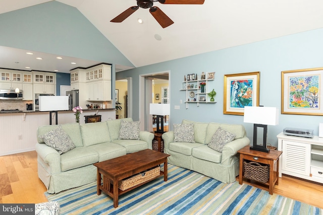 living room featuring ceiling fan, vaulted ceiling, and light wood-type flooring