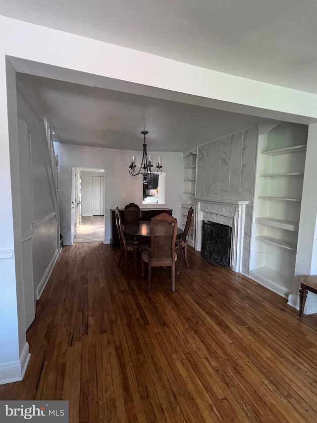 dining area with dark wood-type flooring, an inviting chandelier, a fireplace, and built in shelves