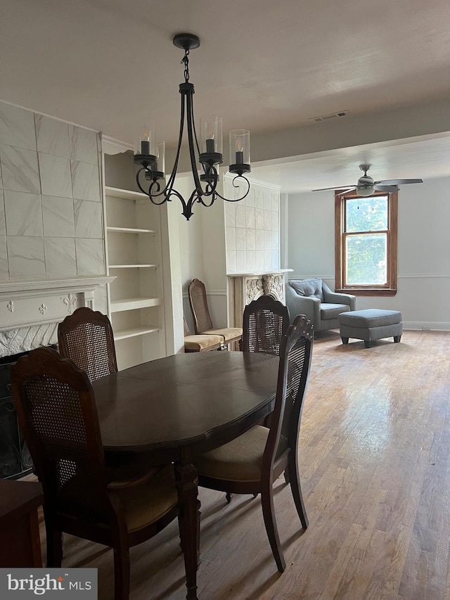 dining area featuring hardwood / wood-style flooring, a premium fireplace, and ceiling fan with notable chandelier