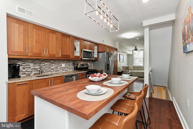 kitchen with sink, dark hardwood / wood-style floors, a breakfast bar area, ceiling fan with notable chandelier, and appliances with stainless steel finishes