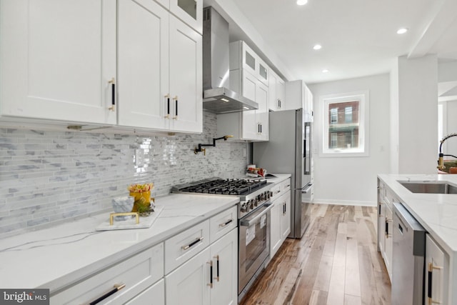 kitchen featuring wall chimney range hood, sink, light hardwood / wood-style floors, white cabinetry, and stainless steel appliances