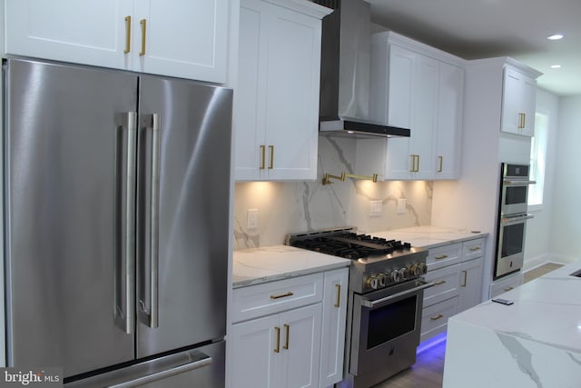 kitchen with light stone countertops, white cabinetry, wall chimney exhaust hood, and stainless steel appliances