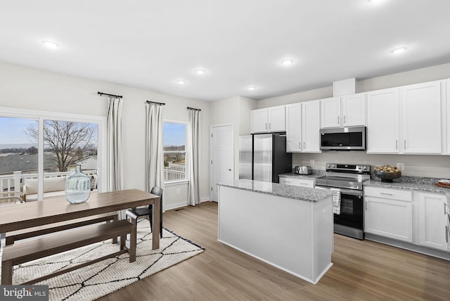 kitchen with white cabinets, light stone counters, stainless steel appliances, and a center island