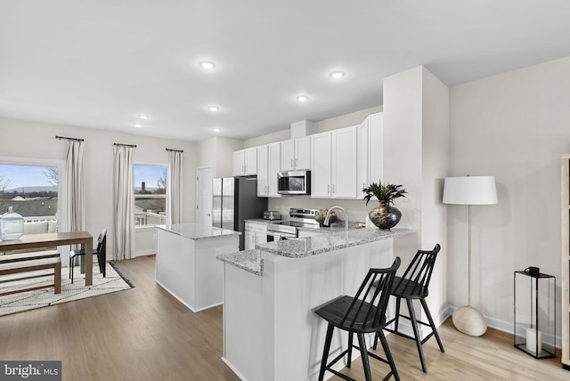 kitchen featuring white cabinetry, kitchen peninsula, appliances with stainless steel finishes, light stone countertops, and a center island