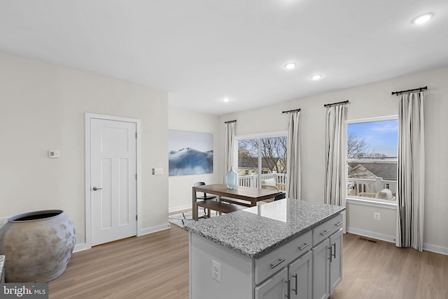 kitchen with light stone countertops, a center island, plenty of natural light, and light hardwood / wood-style floors