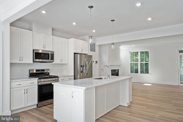 kitchen with pendant lighting, stainless steel appliances, a kitchen island with sink, white cabinets, and sink