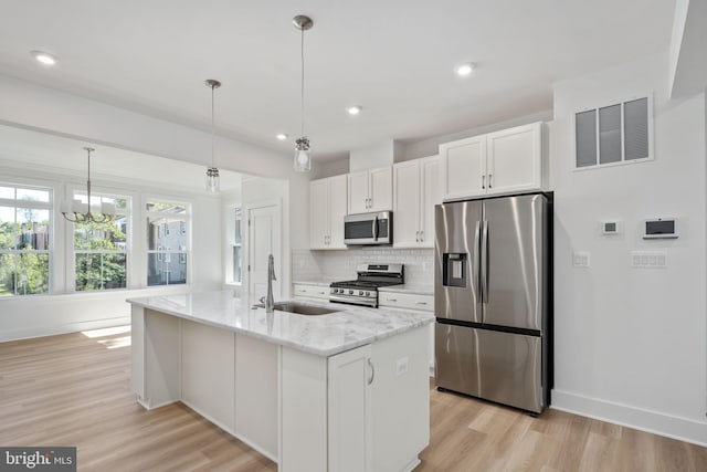 kitchen featuring stainless steel appliances, white cabinetry, an island with sink, and hanging light fixtures