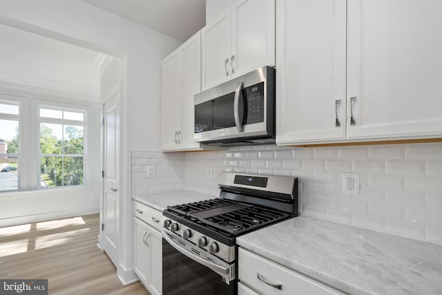 kitchen featuring appliances with stainless steel finishes, light wood-type flooring, light stone countertops, white cabinets, and tasteful backsplash