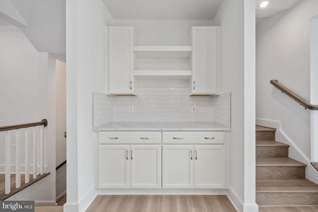 interior space with light hardwood / wood-style flooring, white cabinetry, light stone counters, and decorative backsplash